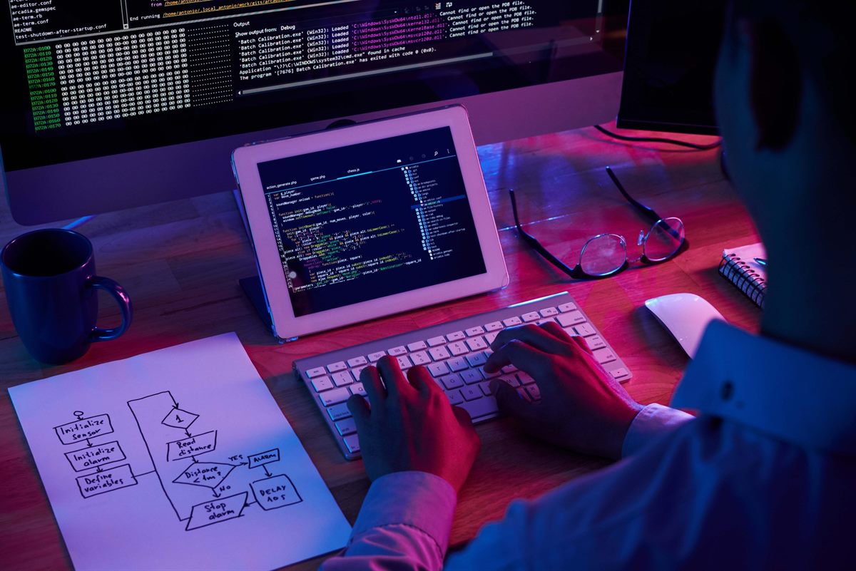 A developer at a desk with code and a system diagram on screen