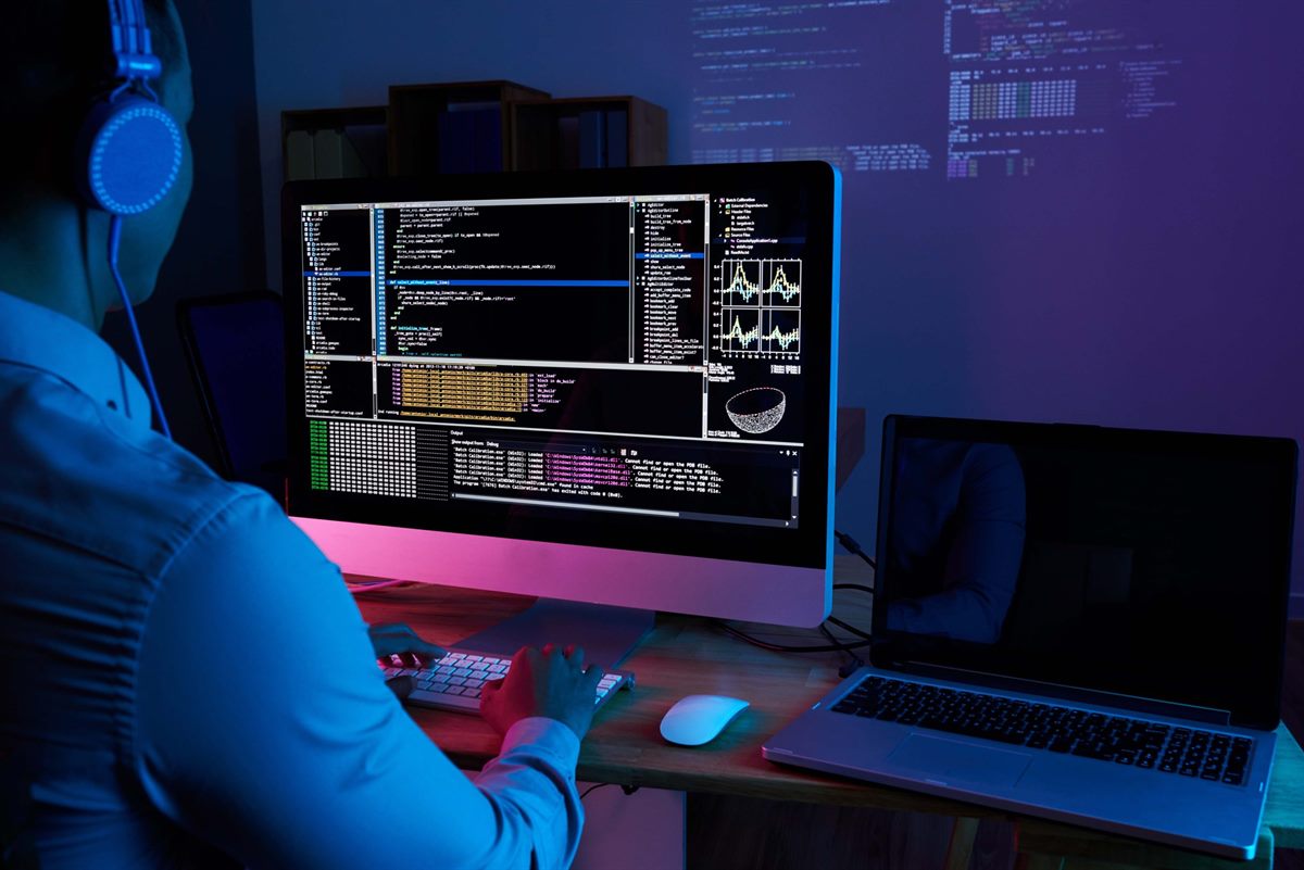 A developer reviewing data on a large monitor beside a laptop